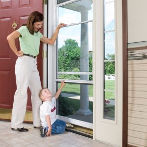 A mom smiled while closing the window of a storm door with her young son