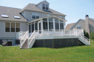 large home with a sunroom and high deck with stairs leading down to grass